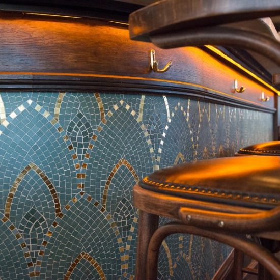 Comptoir en bois et mosaique de la brasserie Le Manfred à Paris avec ses chaises en bois et assises en cuir. Décoration par le Studio Emma Roux